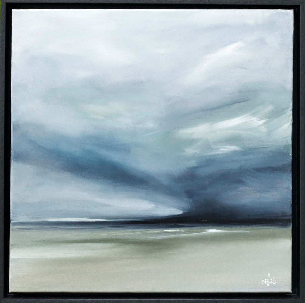 A framed abstract landscape painting featuring a dramatic cloudy sky in shades of blue, gray, and white, meeting a muted beige ground. The artwork is presented in a simple black frame.